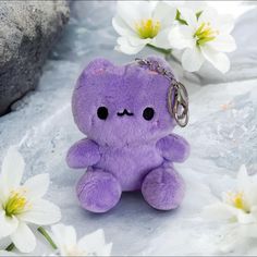 a purple teddy bear keychain sitting next to white flowers on snow covered ground