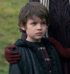 a little boy standing next to a woman in a black and red dress with her arms around him