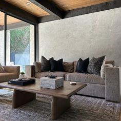 a living room with couches, tables and pillows on the floor in front of large windows