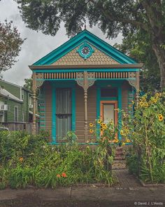 a small blue and orange house with a clock on it's front door in the middle of a garden