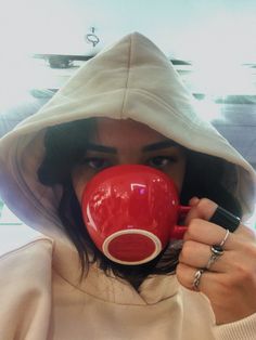 a woman wearing a hoodie and holding a red coffee mug