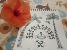 an orange flower sitting on top of a table next to a notebook with drawings and designs