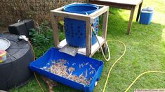 a dog standing next to a blue bucket filled with wood shavings on the grass