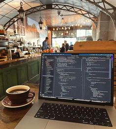 an open laptop computer sitting on top of a wooden table next to a cup of coffee