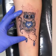 an owl tattoo on the arm with blue eyes and jewels around it's neck