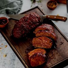 some meat is sitting on a cutting board with sauces and seasonings around it