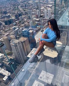 a woman sitting on top of a glass floor in a high rise building looking down at the city