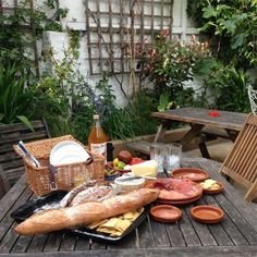 a picnic table with bread, fruit and wine on it in the back yard area