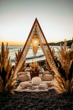 an outdoor seating area with pillows and plants on the ground next to the ocean at sunset