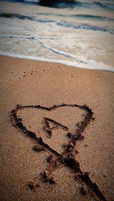 a heart drawn in the sand at the beach with waves coming in to shore behind it