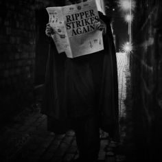 a man in a cape is reading a newspaper while walking down the street at night