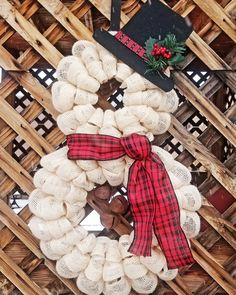 a wreath with a red and black plaid bow on it sitting in front of a wicker wall