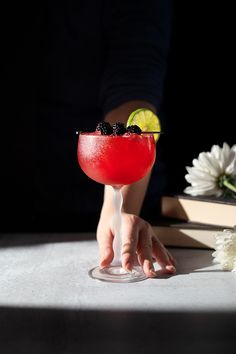 a person holding a drink in front of a table with flowers and books on it