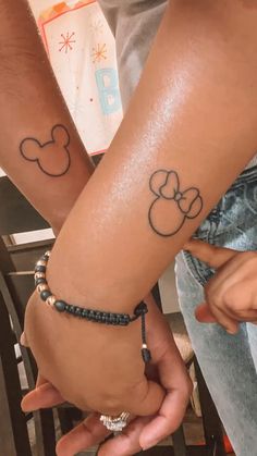 two people are holding hands with tattoos on their arms and wristbands that have mickey mouse heads on them