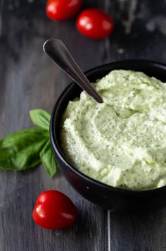 a black bowl filled with pesto and topped with a spoon next to some tomatoes