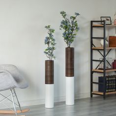 two tall vases with flowers in them are sitting on the floor next to a rocking chair