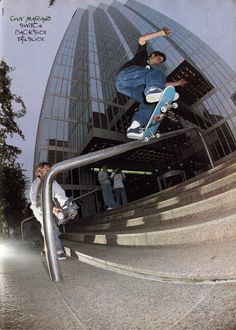 a man riding a skateboard up the side of a metal hand rail in front of a tall building