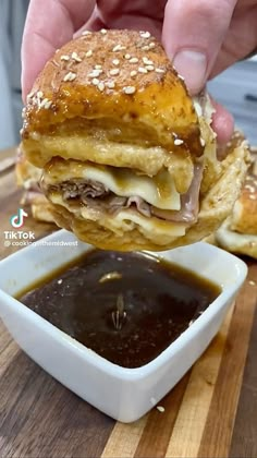 someone is holding up a sandwich in front of a bowl of sauce on a wooden table