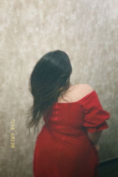 a woman in a red dress is looking at her reflection on the wall behind her