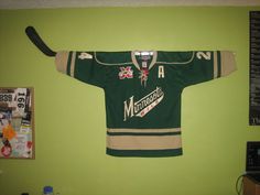 a hockey jersey hanging on the wall in a room with green walls and posters above it