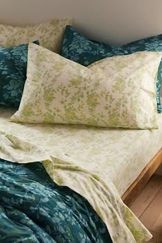 an unmade bed with blue and green comforter on it's headboard