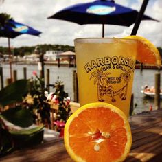 an orange slice next to a glass on a wooden table with umbrellas in the background