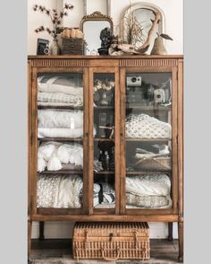 a wooden cabinet with glass doors and baskets on top of it in front of a mirror