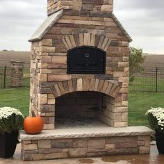 an outdoor brick fireplace with potted plants and pumpkins on the ground next to it