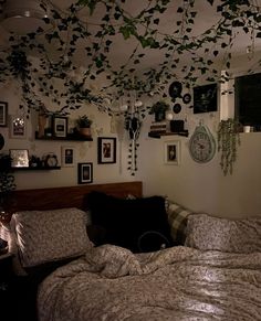 an unmade bed in a room with many pictures on the wall and plants hanging from the ceiling