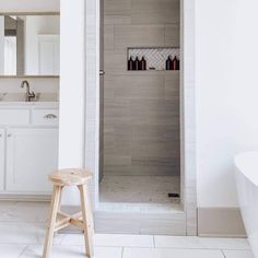 a white bathroom with a wooden stool next to the shower