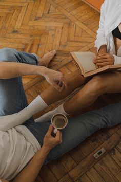 two people sitting on the floor reading books and holding coffee mugs in their hands