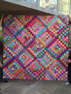 two people holding up a large colorful quilt