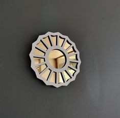 a round mirror mounted to the side of a gray wall next to a light fixture