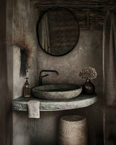 a bathroom sink sitting under a round mirror next to a vase with flowers on it