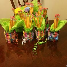 there are many colorful pencils in the cups on the table with ribbons around them