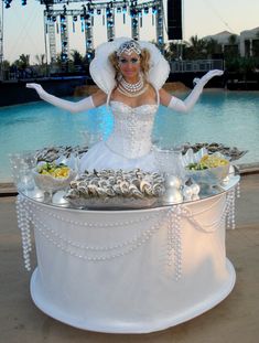 a woman in a white wedding dress sitting on top of a round table with food