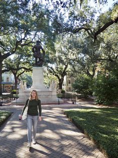 a woman walking down a brick path in front of a statue with trees on both sides