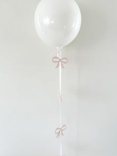 a white balloon with pink bows hanging from it's side on a string in front of a wall