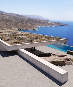 an empty concrete bench overlooking the ocean and mountains in front of a building with a flat roof