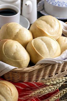 a basket filled with rolls next to two cups of coffee