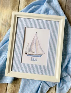 a blue and white sailboat with the word tan in it's center is framed on a wooden surface