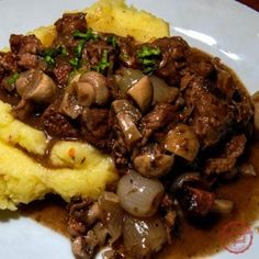 a white plate topped with mashed potatoes and meat covered in mushroom gravy