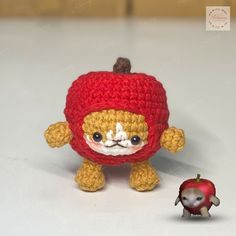 a small crocheted toy is next to a tiny red apple on a table