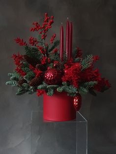 a red vase filled with christmas decorations and candles on top of a glass stand next to a wall