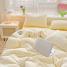 a laptop computer sitting on top of a bed covered in yellow and white striped sheets