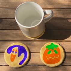 three decorated cookies sitting on top of a wooden table next to a cup of coffee