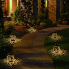 some lights that are sitting in the grass near a house at night with trees and bushes behind them