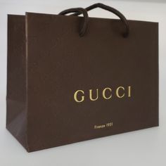 a brown gucci shopping bag sitting on top of a white table next to a wall