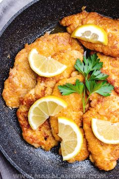 fried chicken with lemons and parsley in a skillet