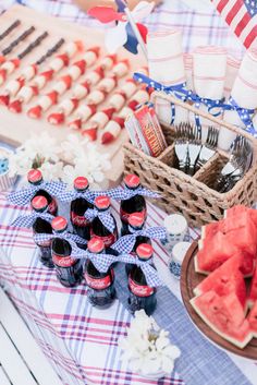 a picnic table with watermelon slices and sodas on it, along with other food items